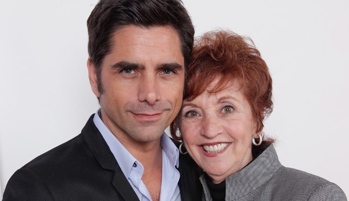 John Stamos wearing a black suit while posing with her mother.